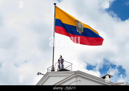 Quito, Ecuador - 27. Oktober 2015: Ein unbekannter Mann auf den Präsidentenpalast während der wöchentliche Wechsel der Wachen mit einer riesigen ecuadorianischen Fahne Stockfoto