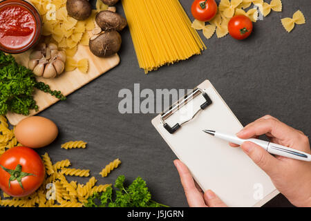 Italienische Spaghetti Foto Rezept. Hand mit Stift schreiben auf weißes Papier auf dem Küchentisch mit Produkten umgeben. Stockfoto