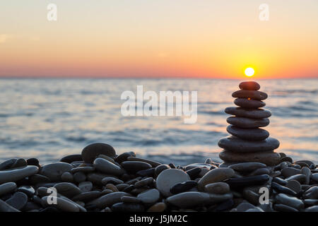 Cairn Steinen gestapelt mit Sonne am steinigen Strand im Sonnenuntergang. Stockfoto