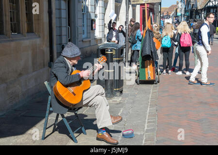 Ein älterer Mann sitzt auf einem Holzstuhl seine Gitarre auf der High Street in Canterbury, Kent. Stockfoto