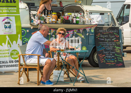 Ein Mann und eine Frau sitzen draußen genießen ein Getränk zur Verfügung gestellt von einem Outdoor-Caterer, die einen VW Campervan zu verkaufen Kuchen und Cocktails umgewandelt hat. Stockfoto