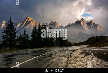 Zielbild Konzept Reisen. Zusammengesetzte Landschaft der hohen Tatra Bergrücken. Kurve Asphaltstraße durch Fichtenwald. Gipfeln beleuchtet von der Sonne in Stockfoto