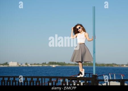 Junge attraktive Mädchen Hipster tanzen auf der Pole. Sie ist ein Top, einen Rock und eine Sonnenbrille tragen. Das Konzept des Lebens in Bewegung. Stockfoto