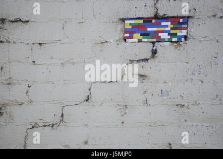 Eine Mauer gemalt weiß und Rissbildung in einem Zick-Zack-Muster hat bunte Lego-artiger Block Spielzeug eingesetzt, wo ein Stein fehlt. Stockfoto