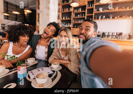 Junger Mann unter Selfie mit Freunden lustige Grimassen in einem Café. Verrückte Jugendliche in einem Café ein Selbstporträt zu machen. Stockfoto