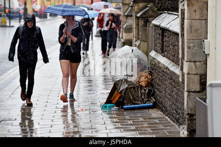 Brighton, UK. 18. Mai 2017. Ein Mann bittet um Geld unter einem Sonnenschirm auf dem Bürgersteig, wie Menschen vorbei in Starkregen im Zentrum von Brighton gehen heute Credit: Simon Dack/Alamy Live News Stockfoto