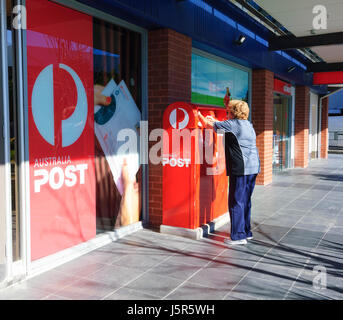 Reife Frau Entsendung einen Brief in einen Briefkasten Australia Post, Shellharbour, New-South.Wales, NSW, Australien Stockfoto