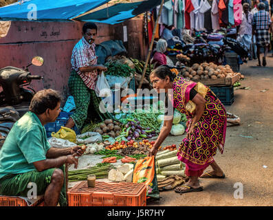 Dame Kleider in der traditionellen indischen Kleid kaufen Gemüse am Markt von Mann in Lungi Tee trinken in Mallappally, Kerala, Indien gekleidet. Stockfoto