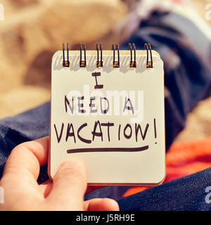 Nahaufnahme eines kaukasischen Jünglings trägt Jeans im Freien zeigt einen Spiral-Notizblock mit dem Text brauche ich einen Urlaub geschrieben Stockfoto