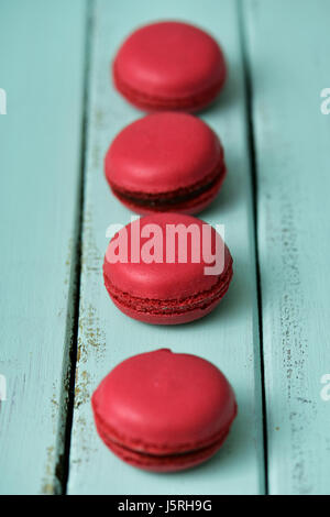 einige appetitlich roten Macarons setzen in der Schlange auf einem blassen Grün rustikalen Holztisch Stockfoto