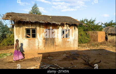 Mädchen zu Fuß Vergangenheit aufgegeben traditionell gebaut Lehmhaus mit Reetdach und Plastikplanen unter dem Rasen in einem ländlichen Dorf in Malawi, Afrika Stockfoto