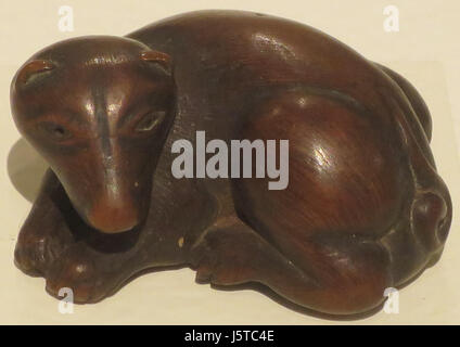 Dieser Netsuke aus dem 18. Und 19. Jahrhundert mit dem Titel „Crouching Male Dog“ ist eine kleine geschnitzte Holzskulptur. Es ist ein bemerkenswertes Beispiel japanischer Handwerkskunst, ausgestellt im Honolulu Museum of Art Stockfoto
