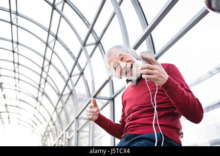 Senior woman mit Smartphone und Kopfhörer im Durchgang. Stockfoto