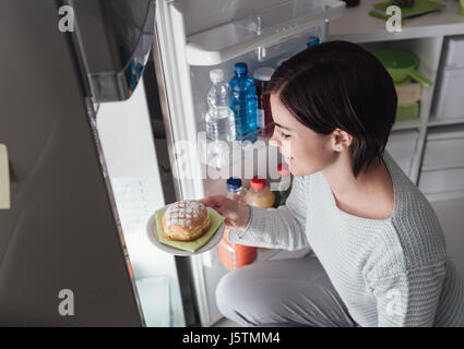 Frau, die eine ungesunde Snacks, sie ist eine köstliche Gebäck aus dem Kühlschrank nehmen Stockfoto