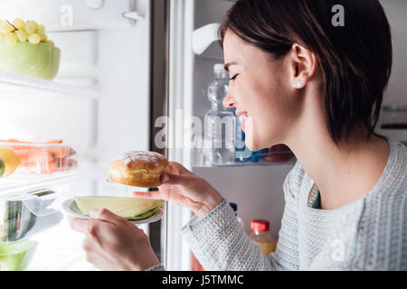 Frau, die eine ungesunde Snacks, sie ist eine köstliche Gebäck aus dem Kühlschrank nehmen Stockfoto