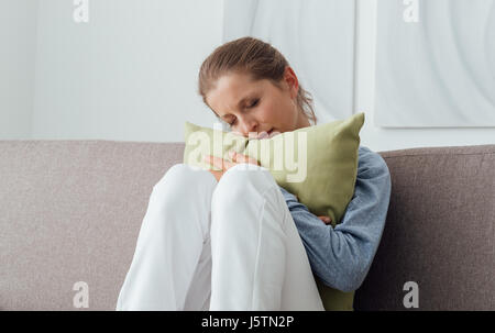 Traurig depressiven Frau zu Hause, ist sie sitzen auf der Couch und umarmt eine Kissen, Einsamkeit und Traurigkeit Konzept Stockfoto