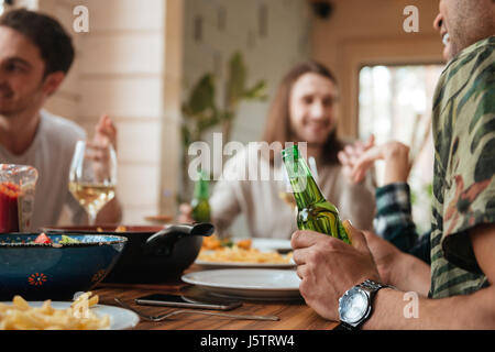 Gruppe der glückliche junge Männer sprechen und trinken Bier am Tisch zu Hause Stockfoto