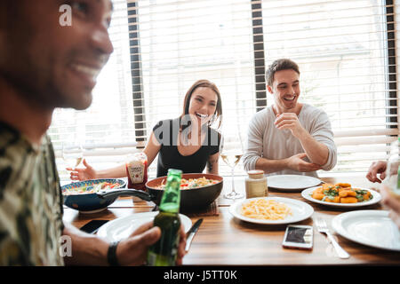 Gruppe von Rassen jungen Freunden genießen Mahlzeit beim Sitzen am Esstisch in der Küche zusammen Stockfoto