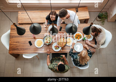 Draufsicht der Gruppe von Menschen, die Abendessen zusammen sitzend am rustikalen Holztisch zu Hause Stockfoto
