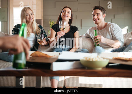 Gruppe von lächelnden jungen Freunde mit Pizza, Wein und Bier sitzen und reden auf sofa Stockfoto