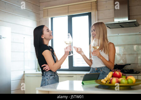 Seitenansicht eines zwei lachende Frauen trinken Wein in der Küche Stockfoto