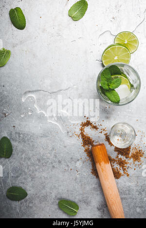 Mojito cocktail Zutaten auf hellgrauen Hintergrund. Limetten, brauner Zucker, hölzerne Saftpresse, Rum und Minze Blätter von oben gesehen Stockfoto