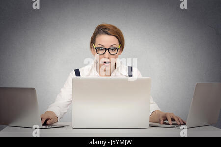 Geschäftige Frau Multitasking versucht, es ganz alleine arbeiten auf mehreren Computern gleichzeitig sitzen am Schreibtisch auf graue Wand Büro Ba verwalten Stockfoto