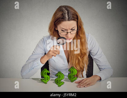 Pfennigfuchser. Geschäftsfrau, die Durchsicht Dollarzeichen Lupensymbol auf Tisch isoliert graue Wand Office-Hintergrund. Finanzielle Wirtschaft wir Stockfoto