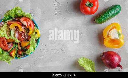 Frisches Gemüse Sommersalat mit Tomaten, Gurken, Paprika, Salat, Zwiebel und Sonnenblumenkerne in blau Schüssel über grauen Beton Hintergrund Stockfoto