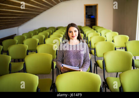 Eine schöne Geschäftsfrau, die allein in einem Hörsaal sitzen Stockfoto