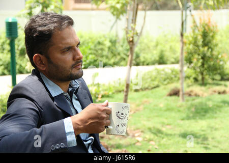 Indische Unternehmen Jüngling sitzen und denken bei einer Tasse Kaffee im Garten Stockfoto