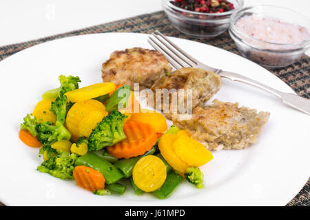 Stücke von Brathähnchen Filet im Teig und Mischung aus gedünstetem Gemüse in weißen Teller. Studio Photo Stockfoto