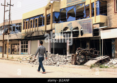 Mosul, Irak. 11. Mai 2017. Ein Fußgänger läuft eine Straße hinunter und Pässe von zerstörten Gebäuden in der christlichen Stadt Stützpunkt in der Nähe von Mosul, Irak, 11. Mai 2017. Darüber bleibt eine Geisterstadt sogar Monate nach der Befreiung. Foto: Jan Kuhlmann/Dpa/Alamy Live News Stockfoto