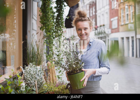 Porträt Lächeln weibliche Floristen halten Topfpflanze am Schaufenster Stockfoto