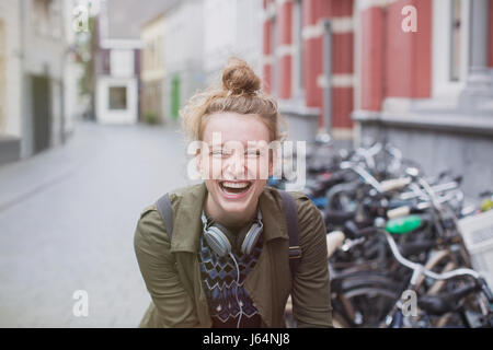 Porträt-begeisterte, junge Frau mit Kopfhörern auf Stadt Straße lachen Stockfoto