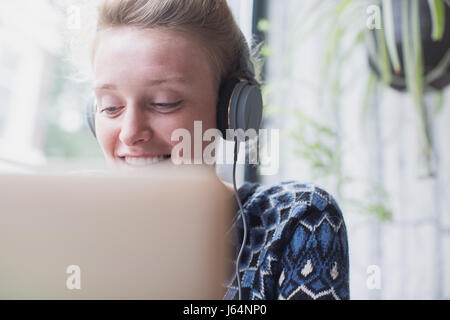 Lächelnde junge Frau mit Kopfhörern mit Laptop im café Stockfoto