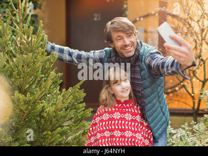 Vater und Tochter nehmen Selfie mit Weihnachtsbaum außerhalb Haus Stockfoto