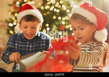 Bruder und Schwester in Santa Hüte Weihnachtsgeschenk öffnen Stockfoto