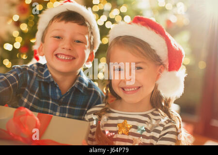 Porträt lächelnd, begeisterten Bruder und Schwester in Santa hüten holding Weihnachtsgeschenk Stockfoto