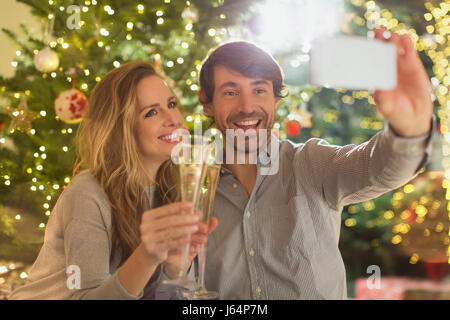 Lächelnde paar Champagner Toasten Flöten und nehmen Selfie vor Weihnachtsbaum Stockfoto