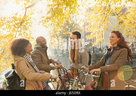Lächelnde junge paar Freunde mit Fahrrädern sprechen unter sonnigen Herbst Baum Stockfoto