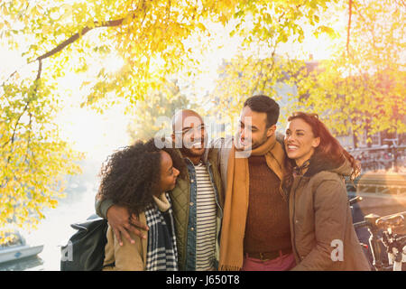 Lächelnde junge Freunde unter sonnigen Herbst Baum umarmen Stockfoto