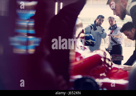 Manager und Formel 1 Rennfahrer, die reden in Werkstatt Stockfoto