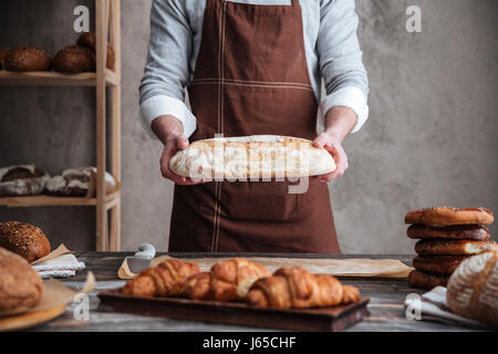 Foto des jungen Mannes Bäcker Bäckerei Brot hält ständigen beschnitten. Stockfoto