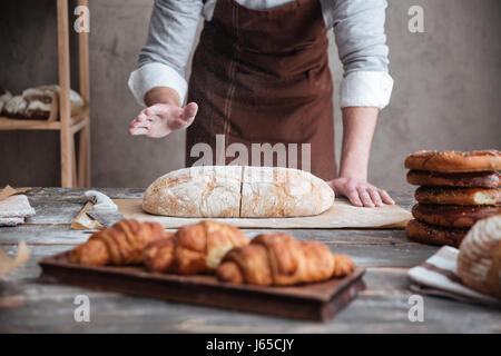 Bild des jungen Mannes Bäcker das Brot schneiden beschnitten. Stockfoto