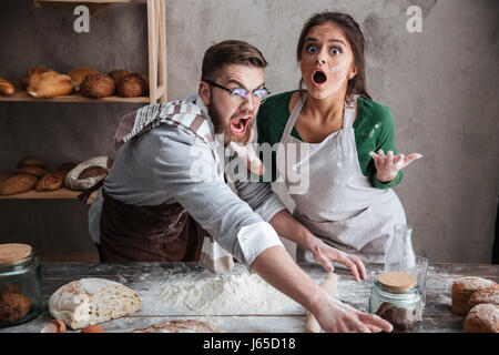 Schockiert Mann und überrascht Frau versucht, etwas auf den Tisch mit Produkten zu fangen Stockfoto