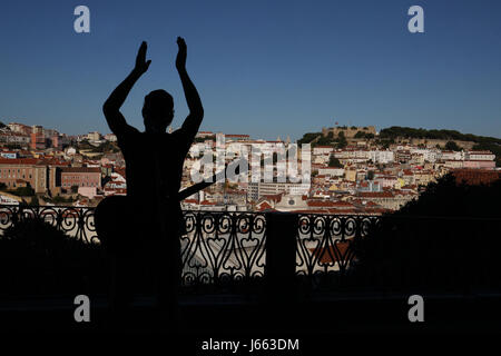 Ansicht der Burg Sao Jorge und Stadtteil Alfama vom Miradouro de San Pedro de Alcantara. Ein Straßenmusikant im Vordergrund. Stockfoto