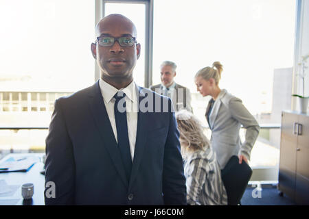 Schwarze Geschäftsmann vor Team sucht ernste und positive Stockfoto