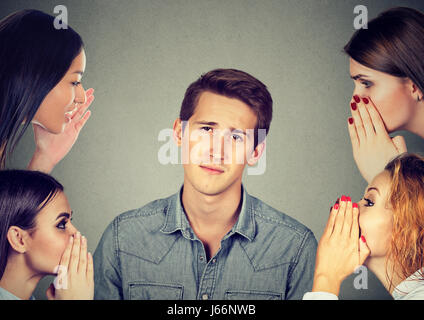 Vier Frauen Flüstern einen geheimen neuesten Klatsch, gelangweilt, genervt Mann Stockfoto