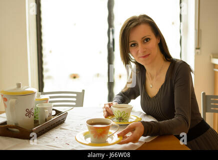 Frau sitzt am Tisch mit einer Tasse Tee Stockfoto